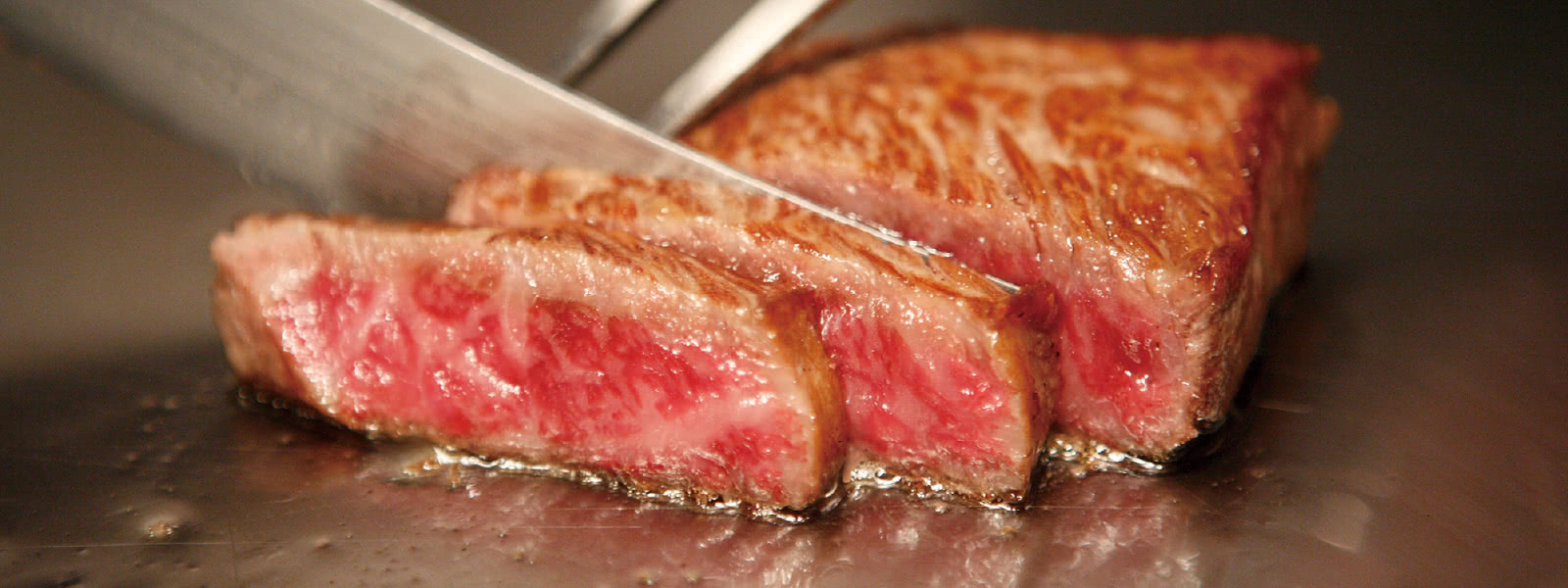 ステーキを鉄板で焼き、ナイフとフォークで切り分けている写真